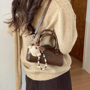 Detail view of dark brown gloss faux leather handbag with cute plush bear charm