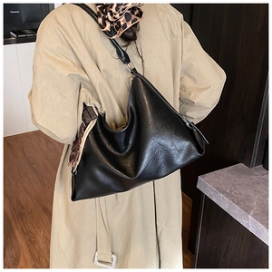 Dettaglio di una grande borsa hobo nera in ecopelle con tracolla larga sopra un trench
