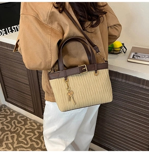 Detail of beige pleated handbag with brown leather trim, gold hardware, and key charm