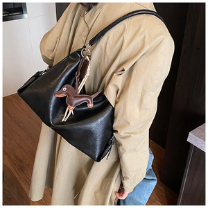 Dettaglio della grande borsa hobo nera con un ciondolo in pelle a forma di bassotto marrone