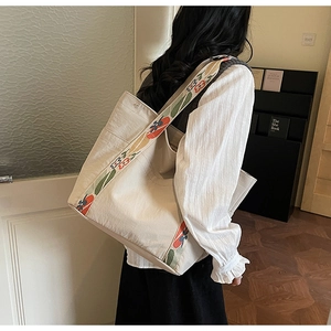 Detailed close-up of beige canvas tote bag featuring vibrant floral embroidered shoulder strap