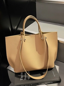 Minimalist beige pebble leather tote bag with dual straps on artistic books