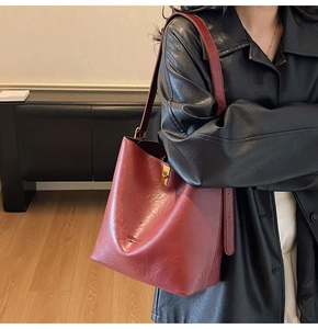 Detail of burgundy leather bucket bag featuring a polished gold twist-lock closure