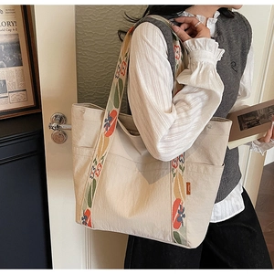 Detail of floral and persimmon embroidered wide straps on a beige canvas tote bag