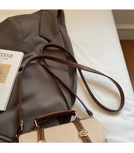 Detail of beige canvas and brown leather crossbody bag with vintage gold clasp on white fabric