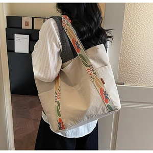 Detail of cream canvas tote bag featuring a floral patterned strap and side pocket