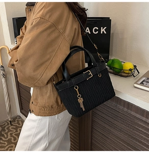 Detail of a black pleated bucket bag with gold hardware worn as a crossbody by a model