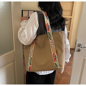 Detail of khaki canvas tote bag featuring floral embroidered strap and side pocket
