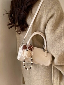 Minimalist beige Boston bag with cute bear charm shown on a shoulder of a model