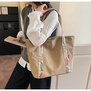 Detail of khaki tote bag featuring floral pattern woven handles and deep front pockets