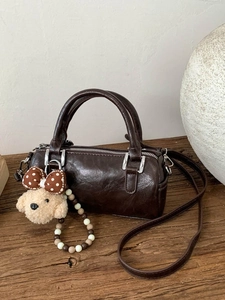 Deep brown cylindrical Boston bag with leather texture and cute puppy charm on wooden surface