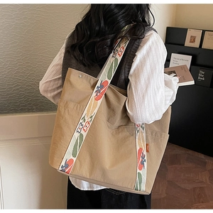 Detail of khaki tote bag with floral wide shoulder strap and orange side label