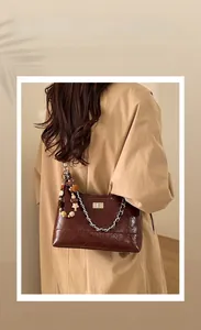 Detail of dark brown quilted leather bag with gold clasp and pearl charm accessory