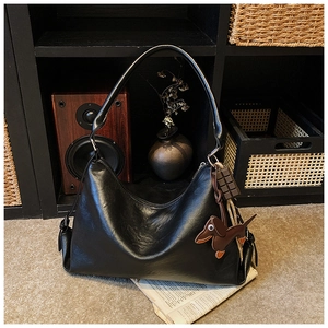 Dettaglio borsa tote in pelle nera con ciondoli bassotto e cioccolato su scaffale in legno