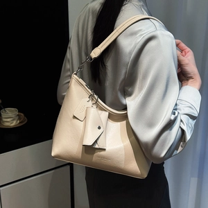 Détail d'un sac cabas beige minimaliste porté avec un haut en satin dans un décor moderne