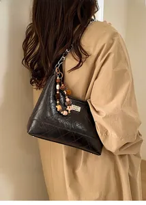 Detail of black quilted hobo bag with chain strap and colorful beaded charm on model