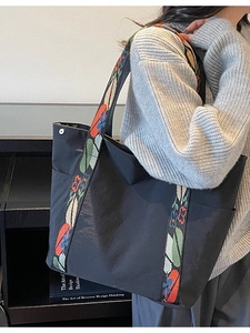 Minimalist black tote bag with colorful embroidered floral strap shown on shoulder