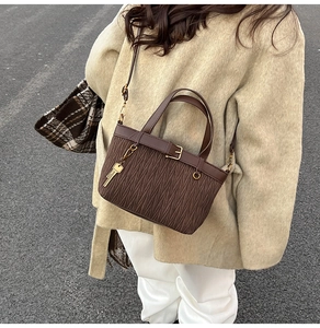 Detail of dark brown pleated bucket bag with gold clasp and key charm on beige coat