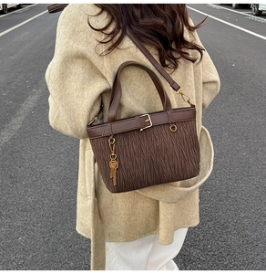 Detail of dark brown pleated bucket bag featuring metallic key pendant and belt-buckle trim