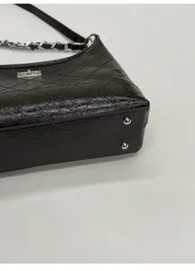 Close-up of a quilted shoulder bag with wide base and protective metal studs