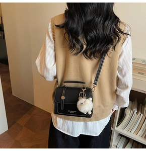 Detail shot of a black leather crossbody bag with sheep charm and metal twist lock closure