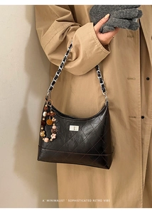 Close-up of black quilted shoulder bag featuring metal chain and colorful beaded charm