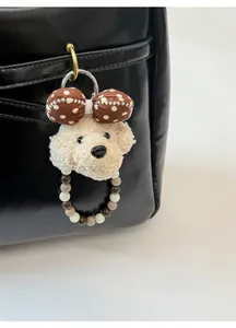 Detail of a plush poodle charm with polka dot bow on a black leather handbag strap