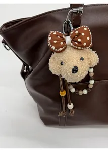 Detailed view of plush dog bag charm with polka dot bow and beaded strap on leather bag