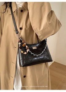 Detail of black quilted patent leather bucket bag with silver chain and colorful charms