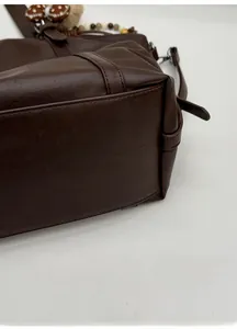 Detailed close-up of the widened sturdy bottom base on this brown leather tote bag