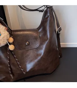 Detail of dark brown leather tote showing texture, flap closure, and plush ball charm