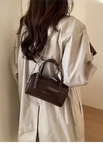 Detail of a dark brown oil wax leather Boston bag with silver chain and top handle strap