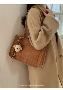 Detail of brown suede tote bag with woven shoulder strap and cute teddy bear charm
