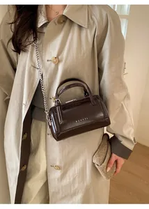 Brown glossy Boston bag with silver chain strap and metal logo in stylish office setting