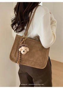 Detail of vintage brown suede shoulder bag with woven edges and teddy bear charm