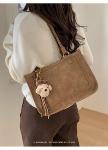 Close-up of brown suede tote bag featuring woven texture details and teddy bear charm