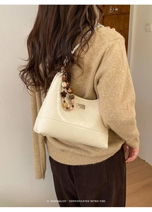 Detail of beige quilted faux leather bag featuring a gold clasp and beaded chain strap