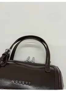 Macro shot of dark brown polished leather bag with MUHETI logo and metallic hardware