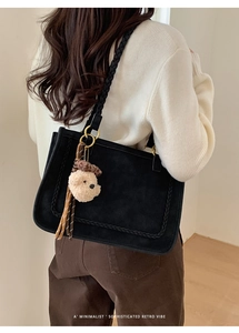 Close-up of black suede tote bag with woven handle and plush bear charm accessory