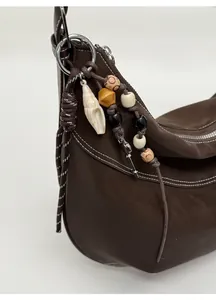 Détail d'un sac en cuir marron vintage avec charms tissés à la main et surpiqûres contrastées
