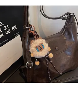 Detailed view of a brown plush bear charm with blue details on a dark leather tote bag