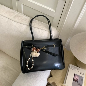 Detail view of black leather tote bag featuring metal ring buckle and bear plush charm