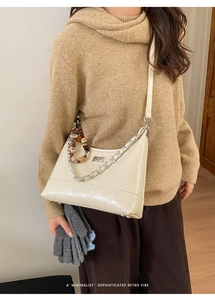 Detail of a creamy white quilted bucket bag with silver chain and artistic beaded charm