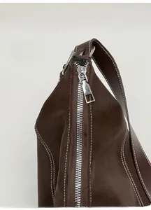 Gros plan du zip argenté et des surpiqûres blanches sur le sac en cuir marron foncé