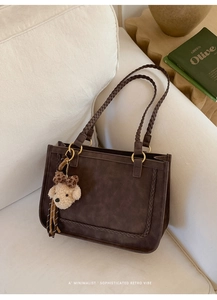 Detail of dark brown suede tote bag with woven shoulder straps and plush bear charm