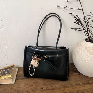 Detail of black faux leather tote bag with plush charm on a rustic wooden table