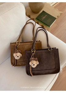 Detail of suede tote bags with woven handles, metal rings, and plush bear charm accessories