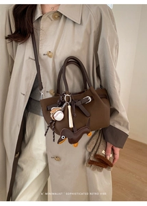 Detail der dunkelbraunen Retro-Beuteltasche mit Hundeanhänger und Baseball-Deko am Mantel
