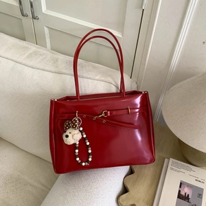 Detail of red faux leather tote bag with gold buckle and cute puppy plush charm on a sofa