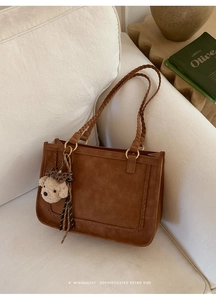 Detail of suede tote bag featuring braided handles and a cute plush bear pendant accessory